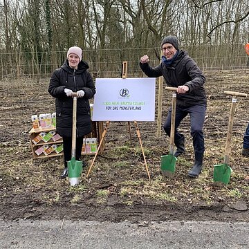 Zwei Personen mit Schaufeln vor einem Wald mit einem Aufsteller mit einem Berief-Plakat, im Hintergrund Berief Getränkekartons.