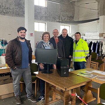 Sachspende für die Ukraine Mitarbeiter in einem Raum mit Sachspenden lächeln in die Kamera.