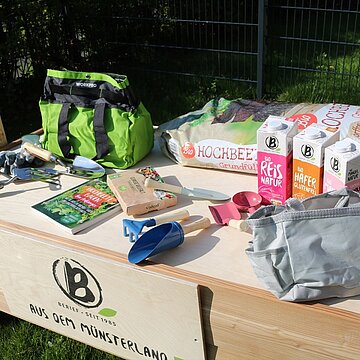 Hochbeet für die Kindertagespflege Eiderdaus Nahaufnahme eines Hochbeets, darauf Berief Getränkekartons sowie Gartenutensilien.