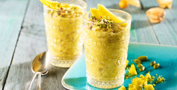 Alles über unseren Haferdrink Zwei Gläser auf einem Holztisch mit einem gelben Getränk und gelben Früchten on top.