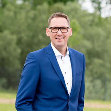 Ein Mann im weißen Hemd und blauem Jacket lächelt in die Kamera.