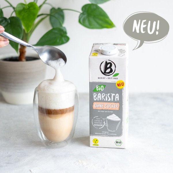 Eine Getränkepackung steht neben einem Cafe Latte vor weißem Hintergrund