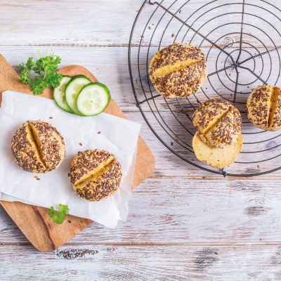 Drei Körnerbrötchen aufgeschnitten auf einem Gitter, weitere auf einem Holzbrett mit Gurkenscheiben
