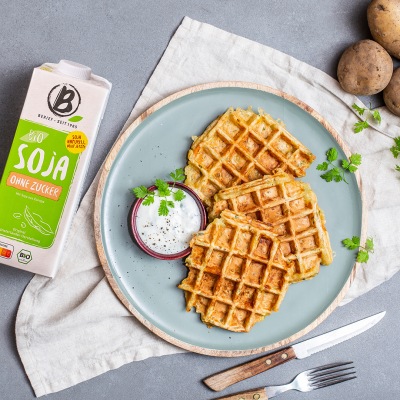 Runde Waffeln zusammen mit einem hellen Dip auf einem hellblauen Teller ganiert mit Kräutern