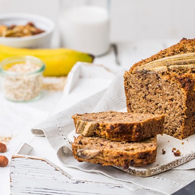 Angeschnittenes Bananenbrot auf einem weißen Tischtuch mit Dekoration