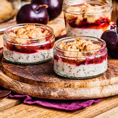 Zwei Pudding-Desserts mit Topping in Glasschalen auf einem Holzteller mit Dekoration