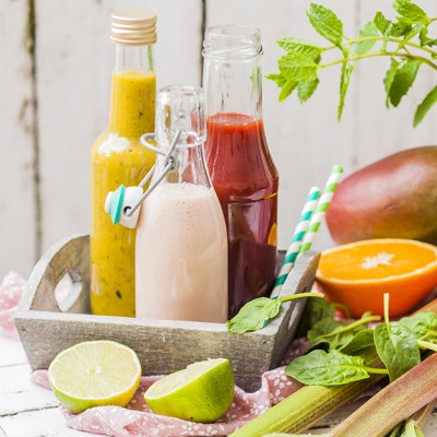 Glasflaschen mit verschiedenfarbenen Smoothies auf einem Tablett mit Obstdekoration