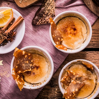 Dessertcreme in kleinen, weißen Schalen mit Zimtstangen auf einem rosa Tischtuch