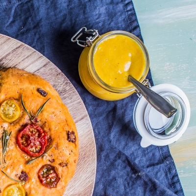 Mango-Curry-Dip neben einem Fladenbrot in einem Glas auf blauem Tischtuch