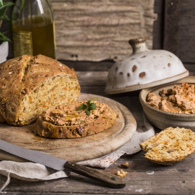 Aufgeschnittenes, helles Brot mit Aufstrich auf einem runden Holzteller.