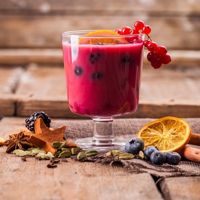 Rotes Getränk mit roten Beeren in einem Glas auf einem Holzbrett.