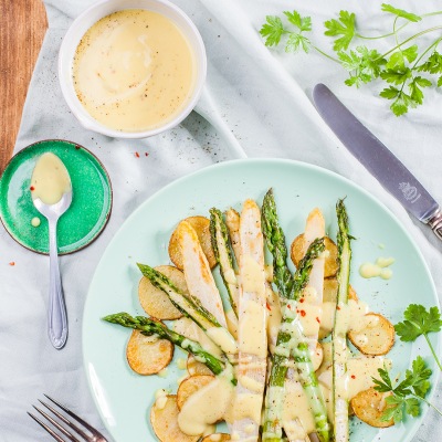 Spargel auf Kartoffelscheiben mit heller Sauce auf einem Teller mit Petersiele