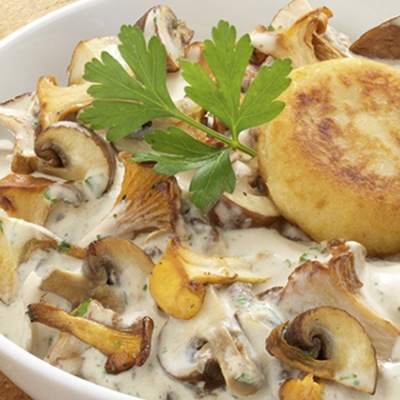 Helle Pilzsuppe mit einem Kartoffeltaler in einer Schüssel mit Petersilie. 