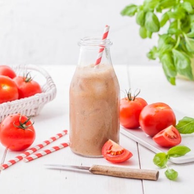 Hellrotes Getränk in einer Glasflasche mit Strohhalm mit Tomaten und Basilikum-Dekoration.