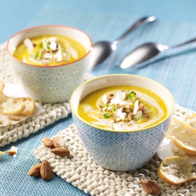 Gelbe Suppe in zwei Schalen mit Mandeltopping und Dekoration